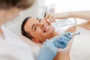 Smiling young man receiving a cosmetic Botox injection from a professional cosmetologist, representing non-surgical facial rejuvenation and modern aesthetic treatments for men
